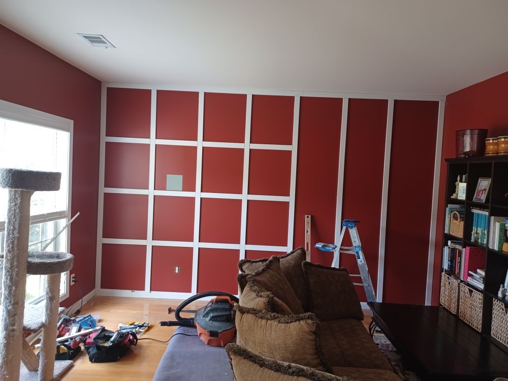 Red accent wall with white trim grid, tools, couch, bookcase.
