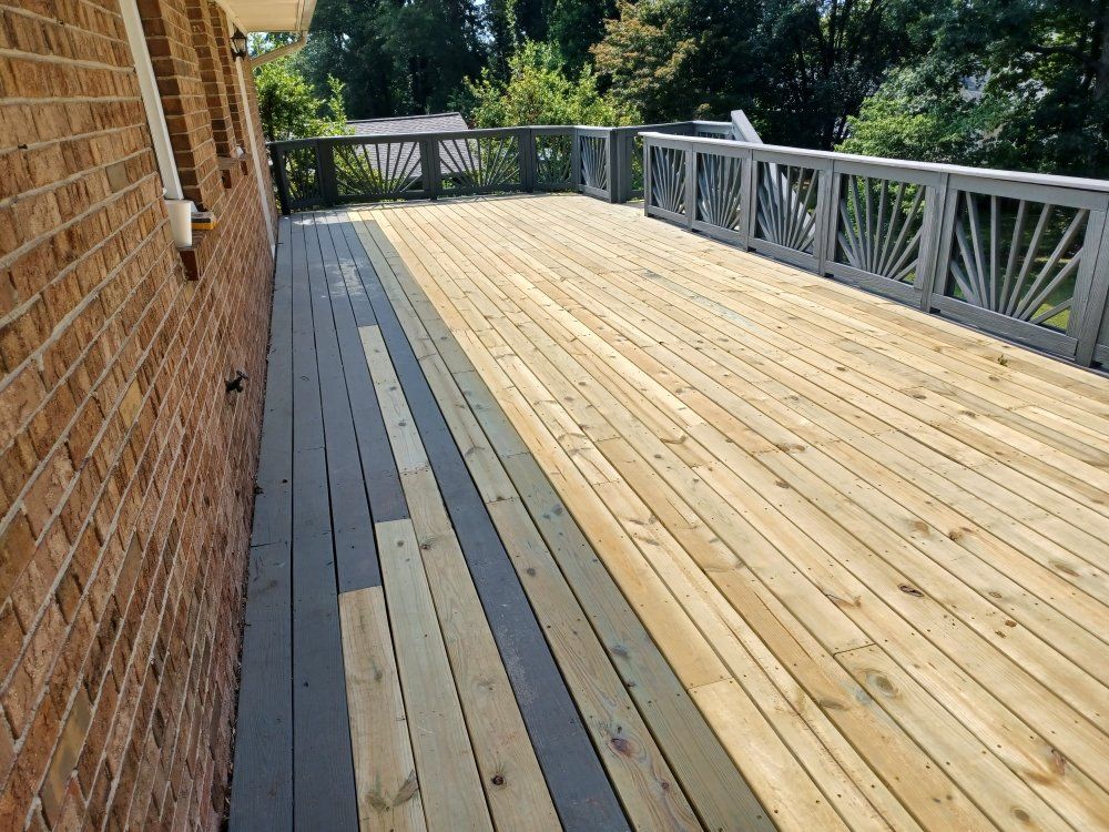 Wooden deck with gray and natural wood planks next to a brick wall. Gray railing with sunburst design.