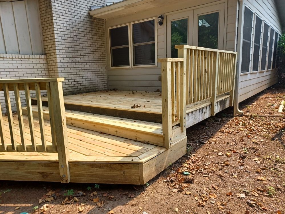 Wooden deck with stairs, railing, and a view of a screened-in porch. The deck is next to a brick building.