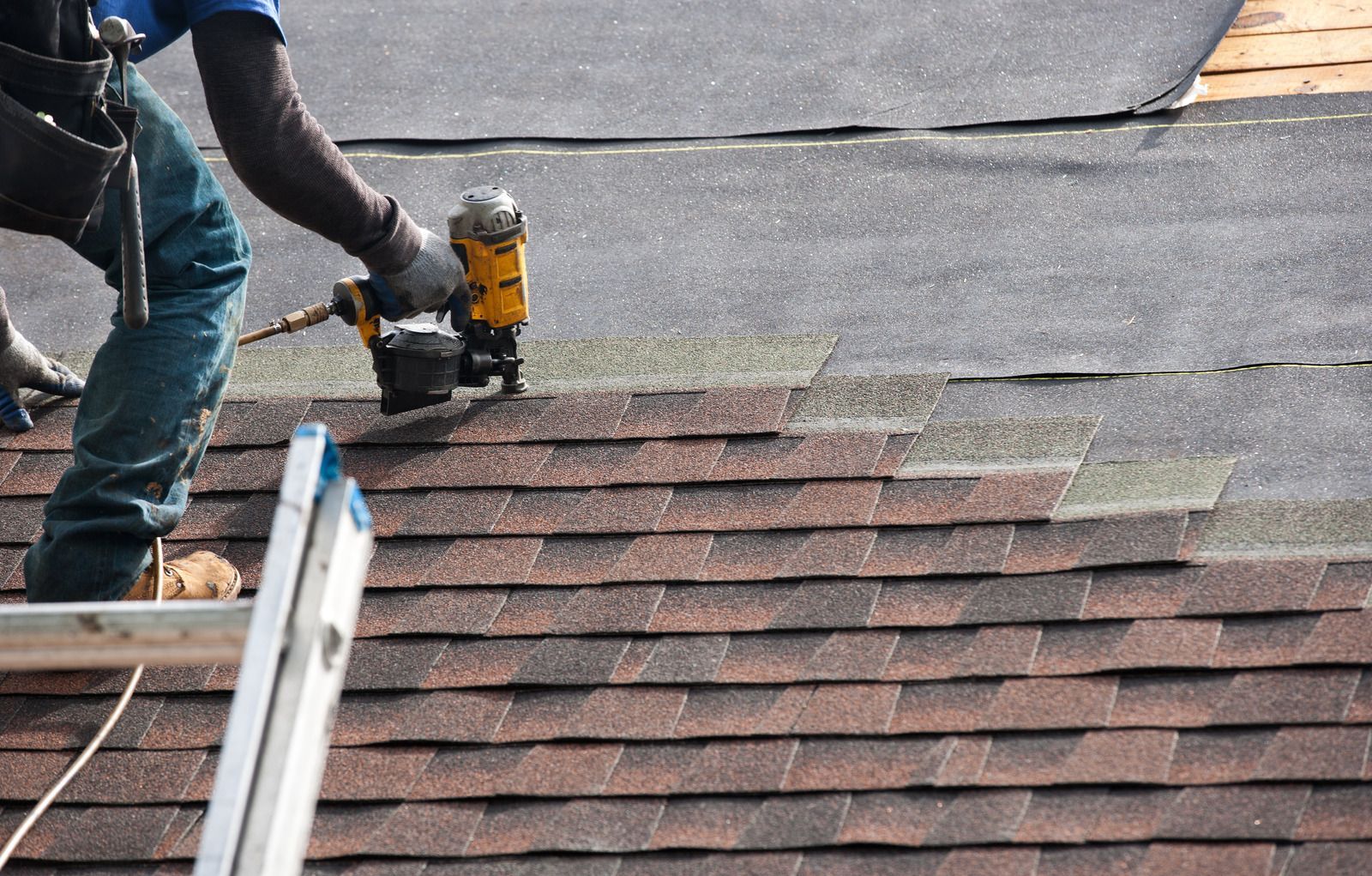 Roofer using a nail gun to install asphalt shingles on a roof.