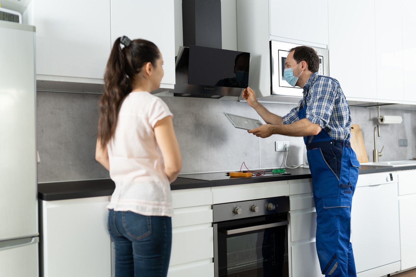 Woman watches a repairman with a tablet in a kitchen, assessing a range hood.