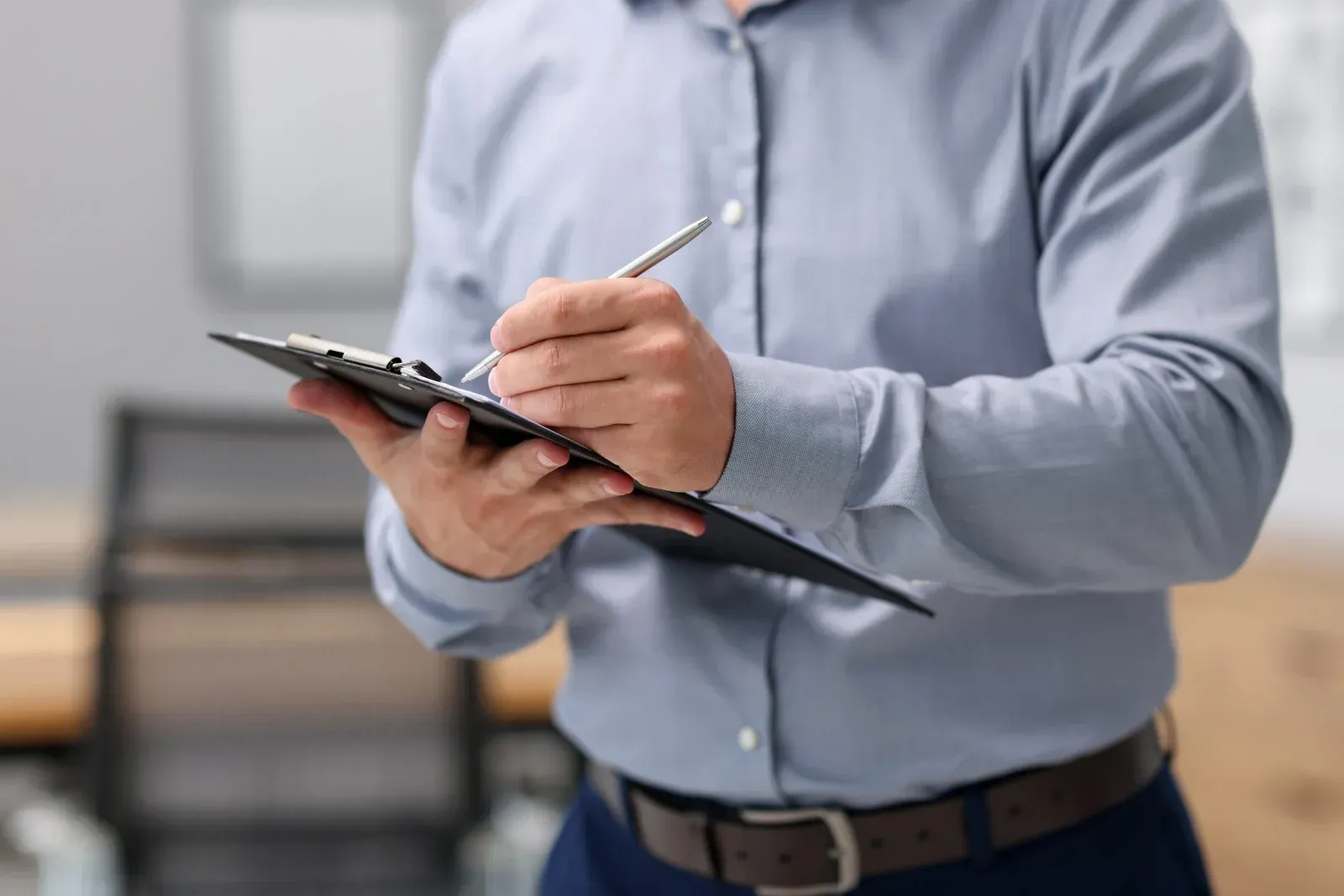 Person in a light blue shirt writing on a clipboard indoors