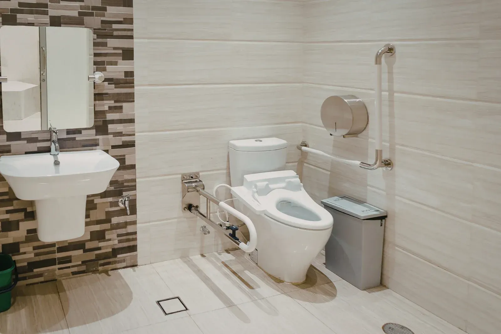 Accessible bathroom with a toilet, wall-mounted sink, grab bars, and tiled walls