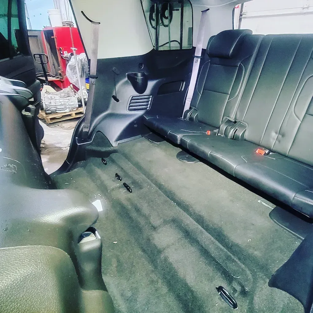 Interior of a vehicle with a folded rear seat, black upholstery, and a carpeted cargo area in a warehouse setting.