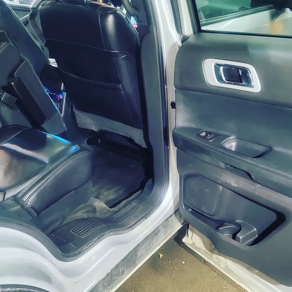 An open rear door of a vehicle showing black leather seats, a dark interior, and a metallic door handle.