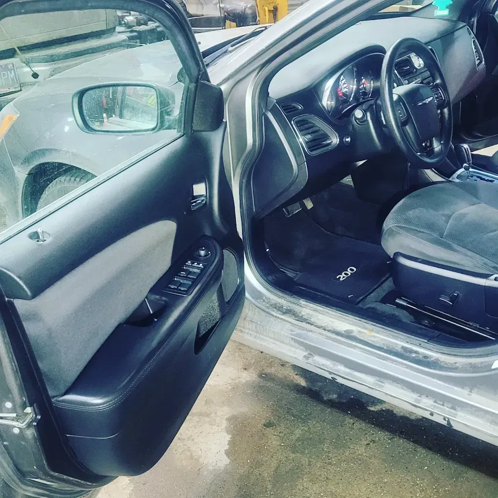 Interior view of a gray car's driver side, showing an open door, steering wheel, dashboard, and a floor mat labeled 200.
