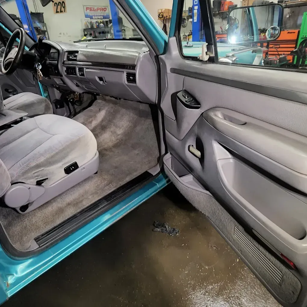 Interior of a teal truck with light gray cloth seats, dashboard, and door panels, viewed from the open driver's door.