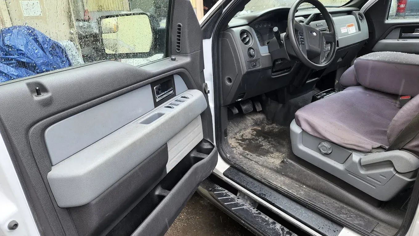 Interior view of a light-colored truck with the driver's side door open, showing gray upholstery and a steering wheel.