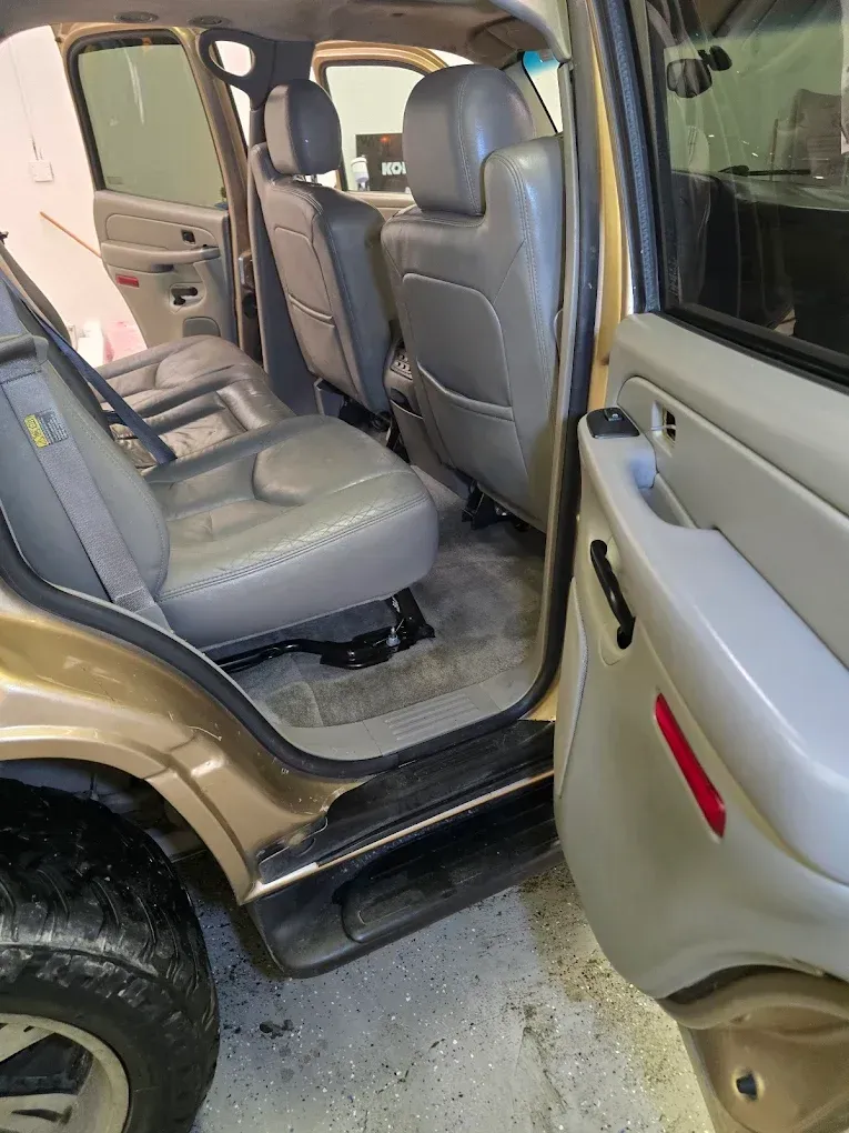 The open rear door of a tan vehicle reveals light gray leather interior seating and tan carpeting.