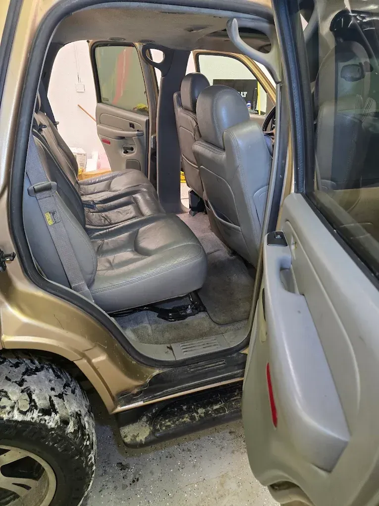 An open side door reveals the tan interior of a vehicle with gray leather seats and floor mats.