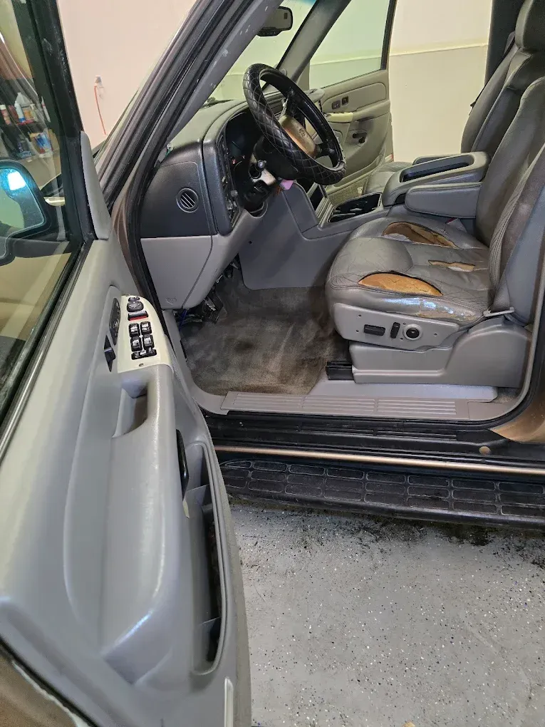 Interior of a vehicle featuring a grey dashboard, steering wheel with a black cover, and worn grey leather driver seat.