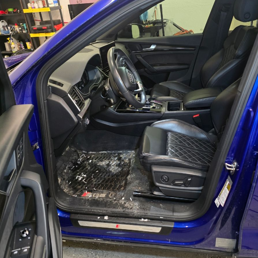Blue car interior with open driver’s door, showing black seats and steering wheel.