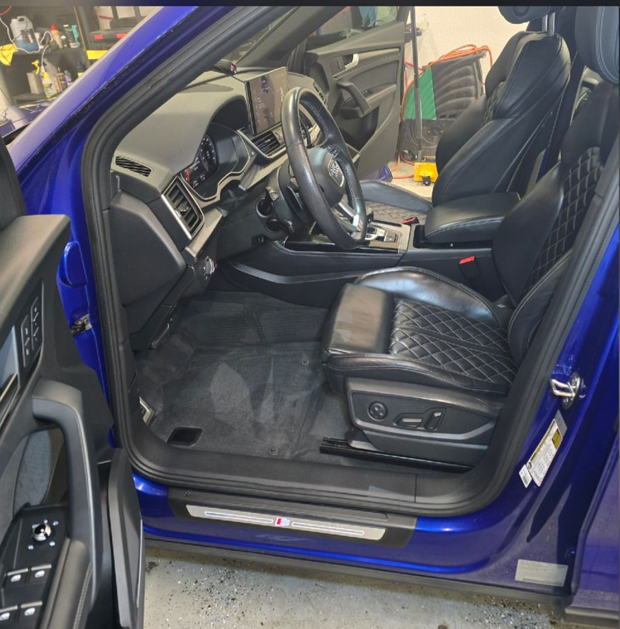 Open car door showing a blue car's black leather driver seat and dashboard interior.