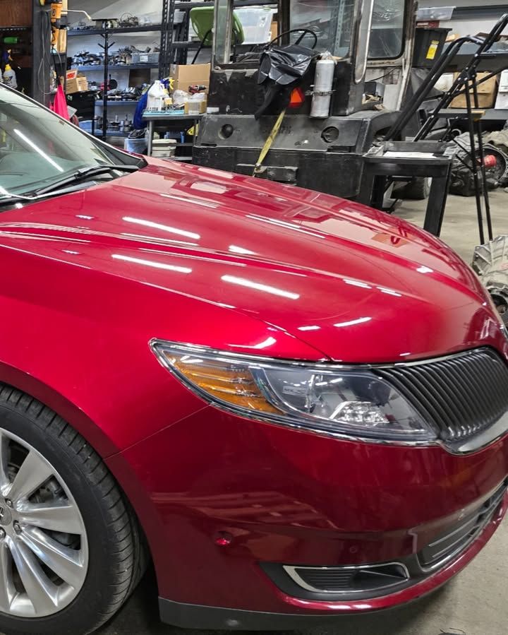 Red sedan in an auto repair shop, showing the front passenger side.
