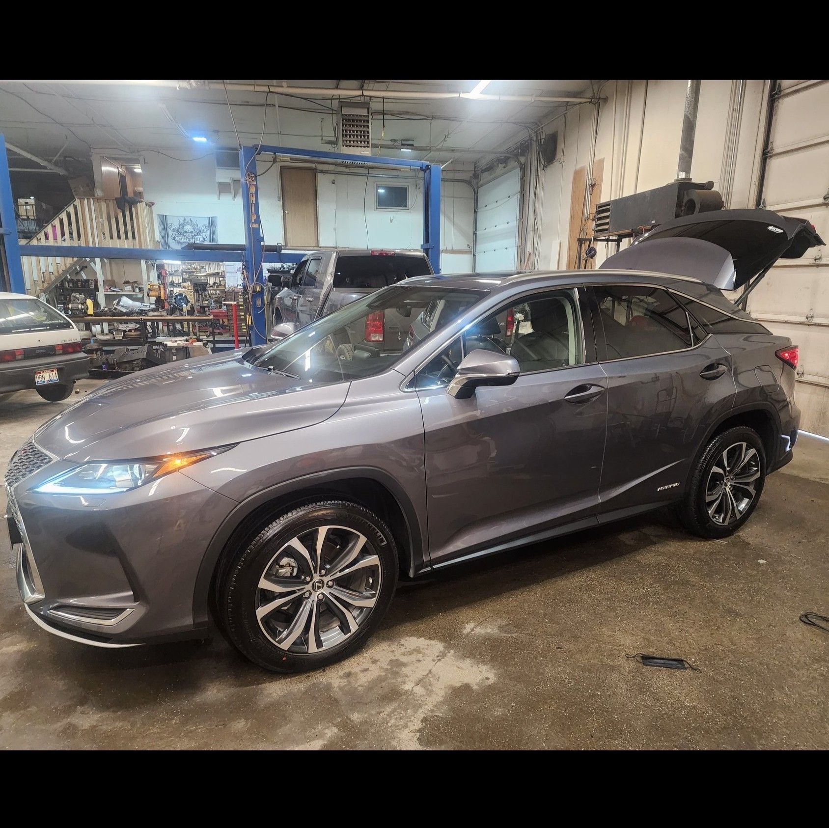 Gray SUV in an auto shop with its rear hatch open, wet floor and repair equipment nearby.