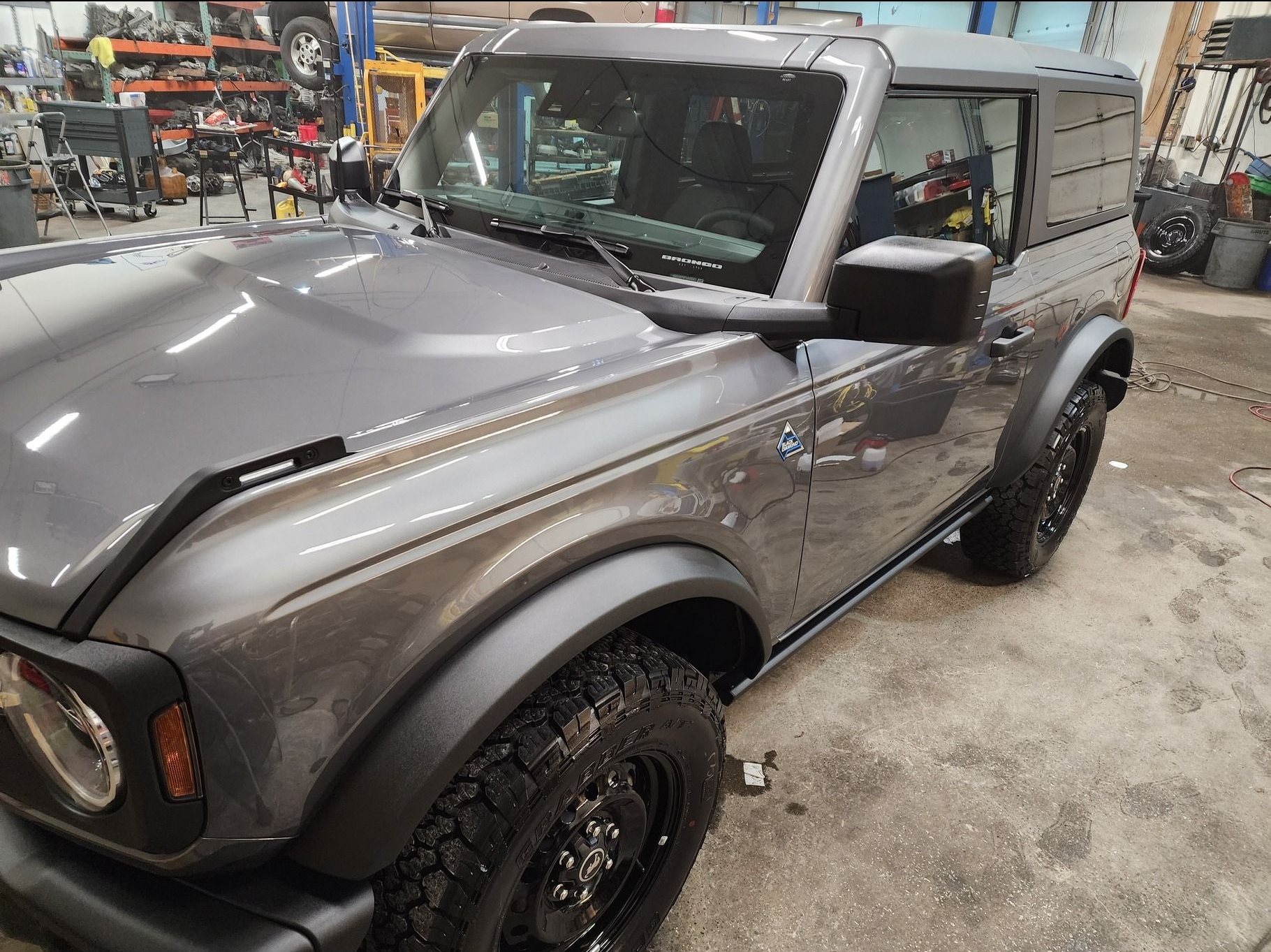 Gray Ford Bronco in an auto shop, front-left view with large off-road tires.