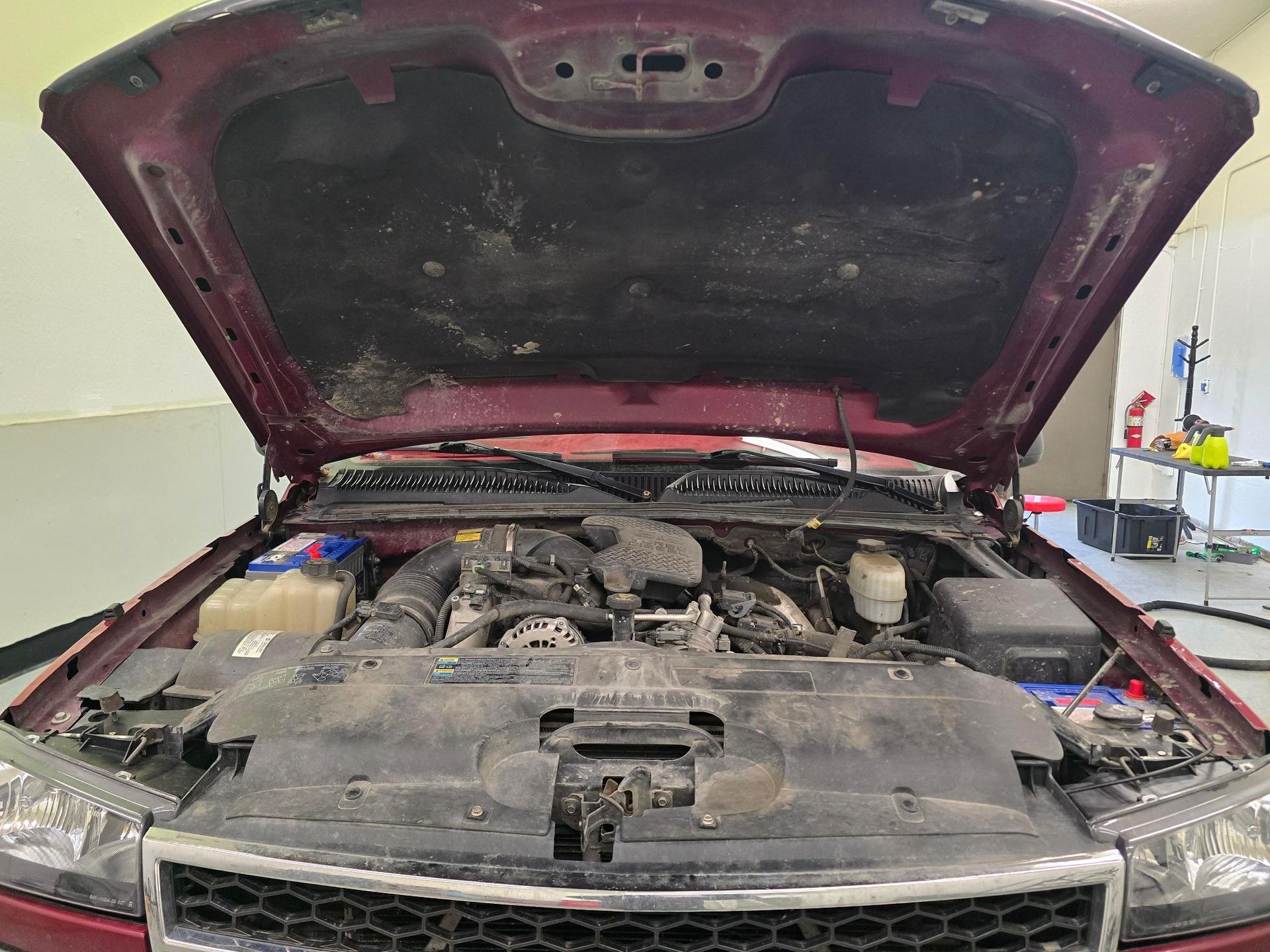 Open car hood showing a dusty engine bay in a garage.