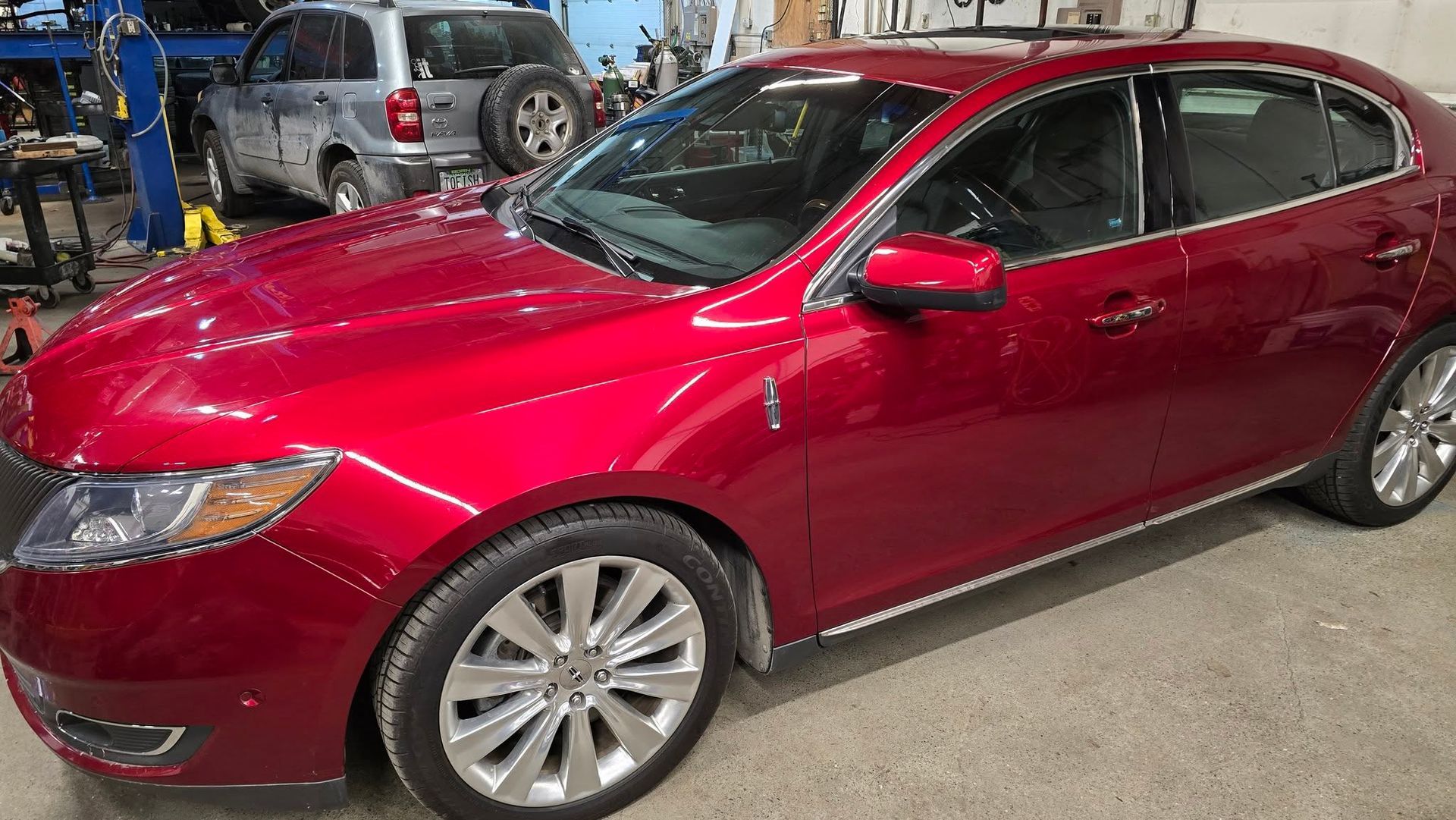 Red sedan parked in a garage, shown from the front-left side.