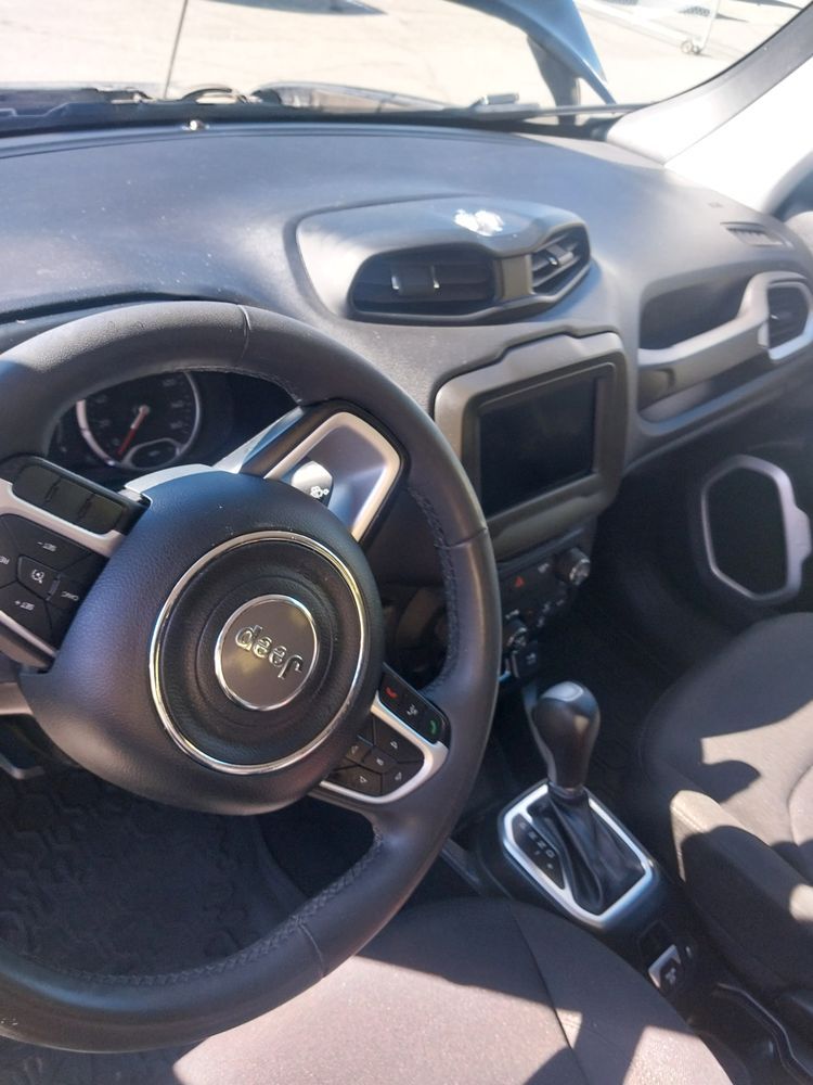Driver's perspective of a black Jeep interior, showing the steering wheel, dashboard, infotainment screen, and gear shift.