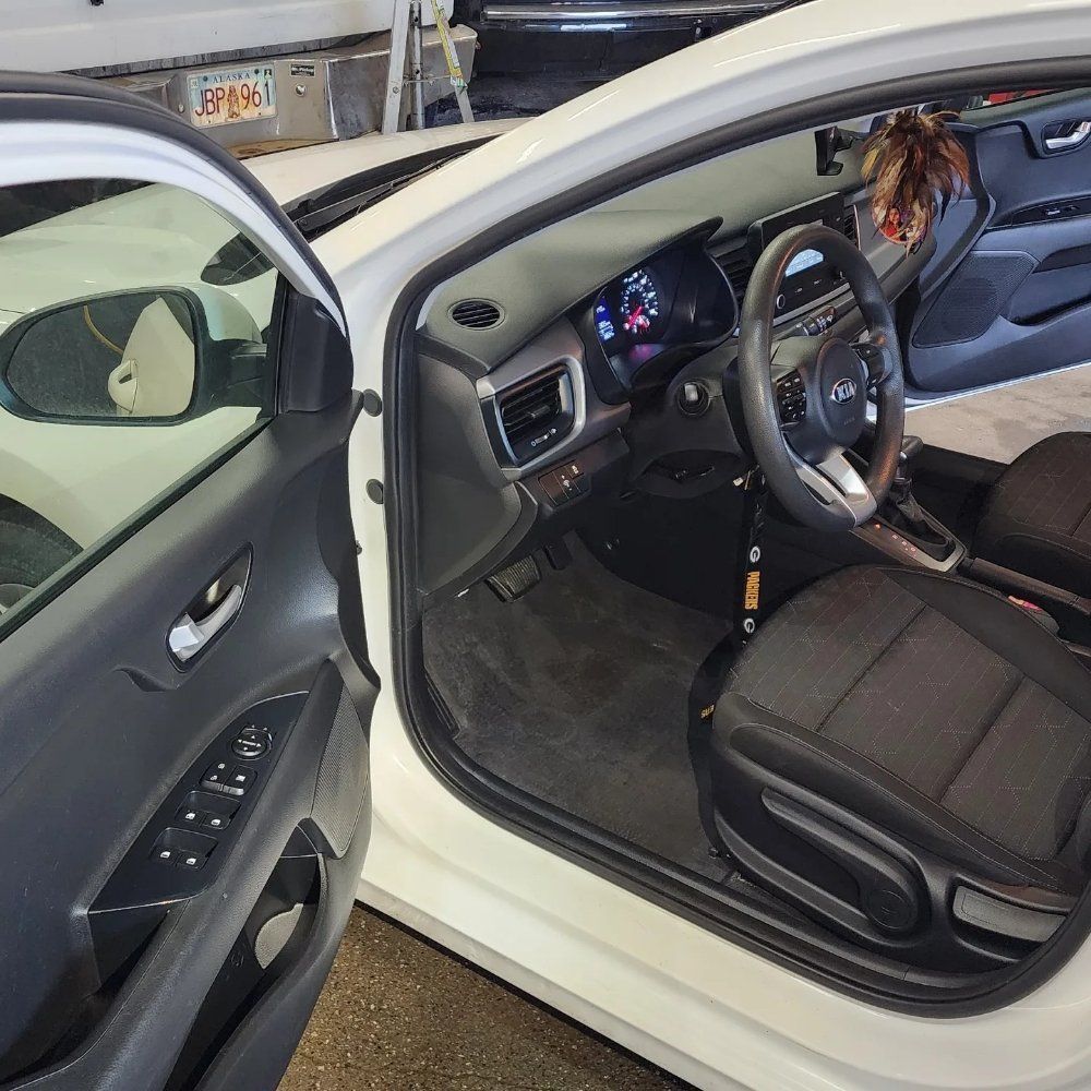 Interior view of a white car with a black driver's seat, steering wheel, and open door, parked in a garage.