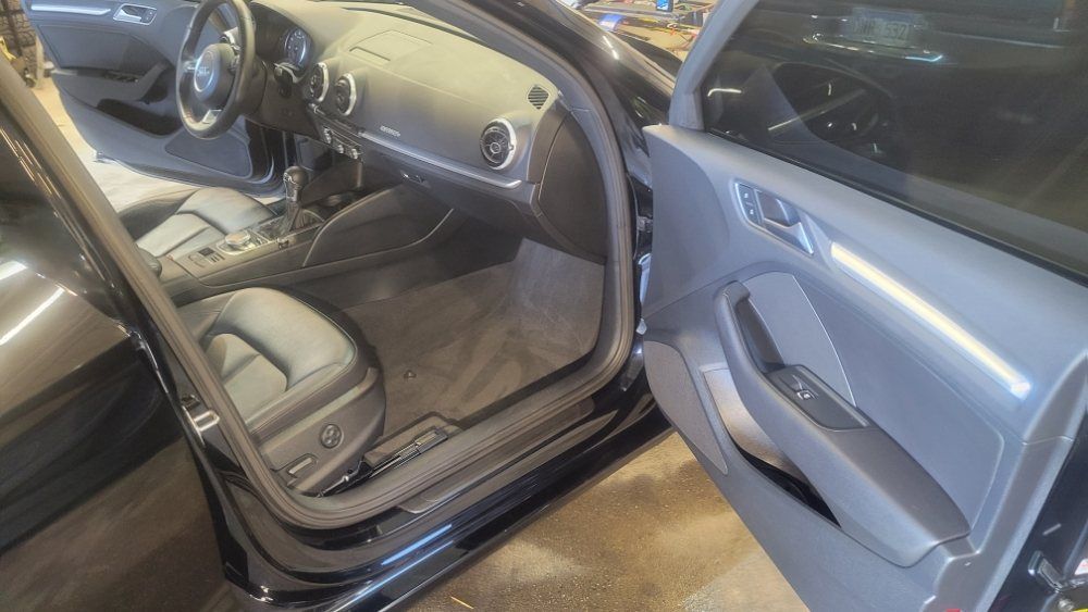 A view into the front interior of a car with dark leather seats, a dashboard with circular vents, and an open side door.