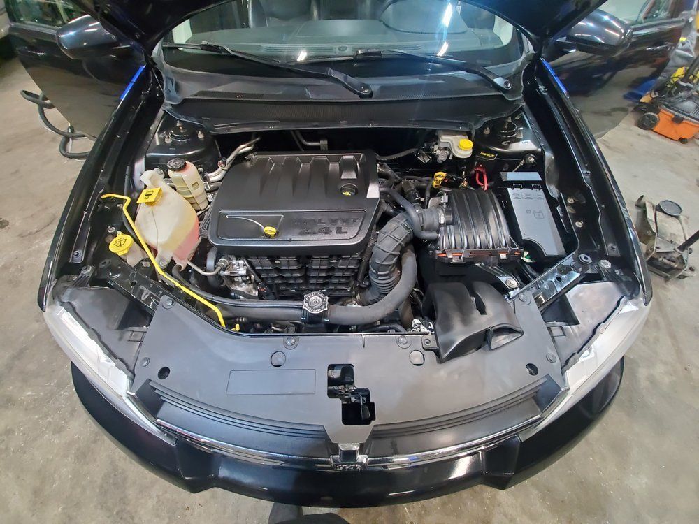 A high-angle view of an open car hood showing the engine bay of a black vehicle inside a garage.