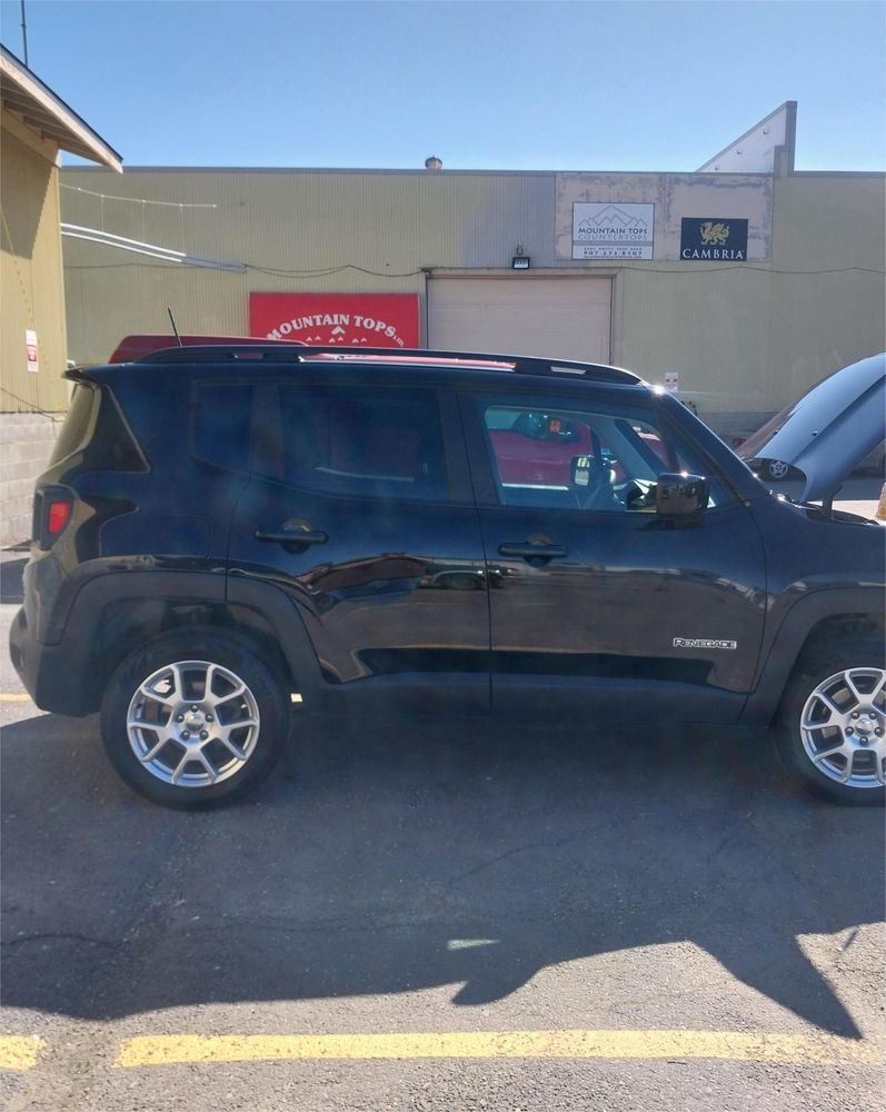 A black Jeep Renegade parked outside a building with a red sign, seen from the side with its hood open.