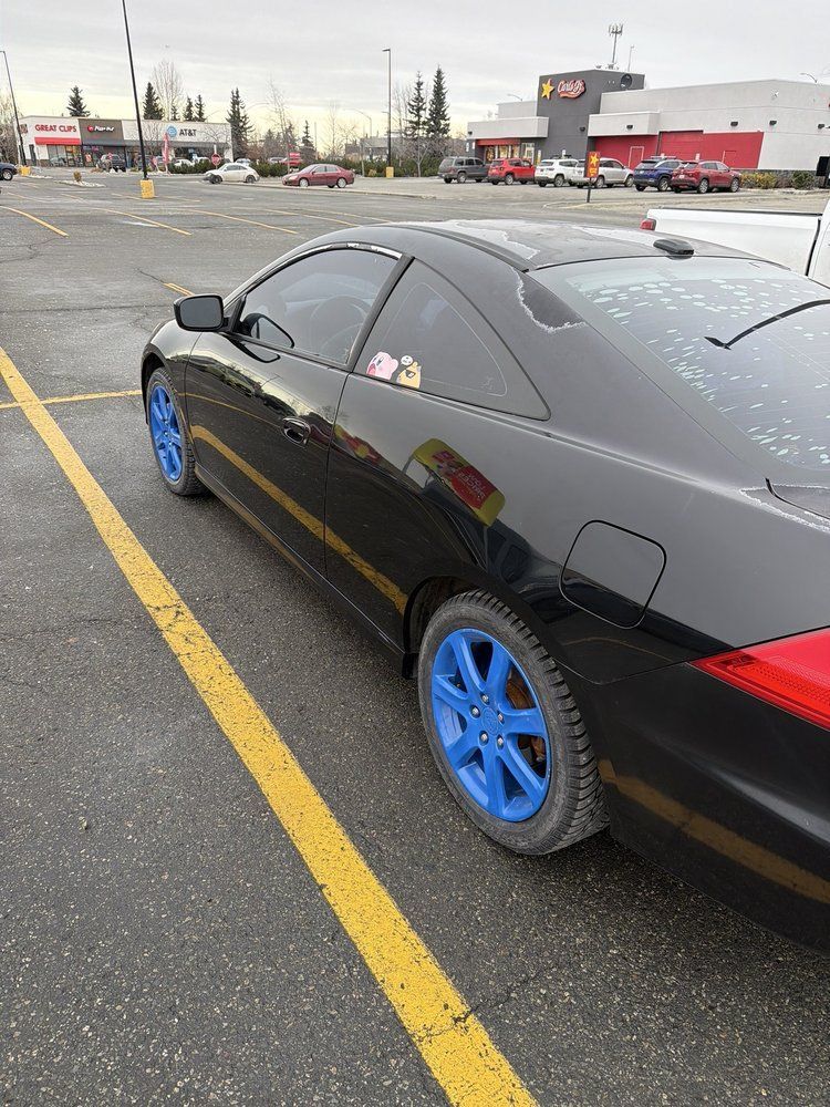 A black two-door coupe with bright blue rims parked in a parking lot on an overcast day.