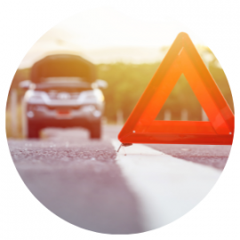 A red warning triangle on a road, a car with an open hood in the background.