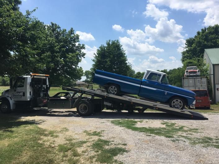 Blue and white classic pickup truck being towed by a tow truck on a sunny day.