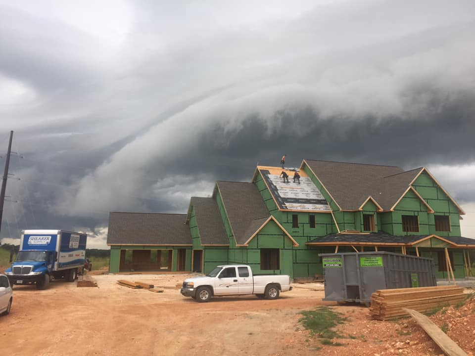 Green building and trucks on a muddy road beneath dark storm clouds