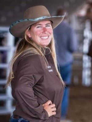 A woman wearing a cowboy hat and a brown shirt is smiling.