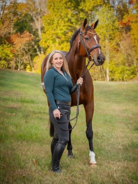 A woman is standing next to a brown horse in a field.