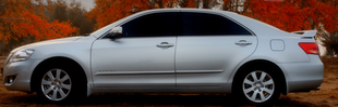 A silver car is parked in a field with trees in the background.