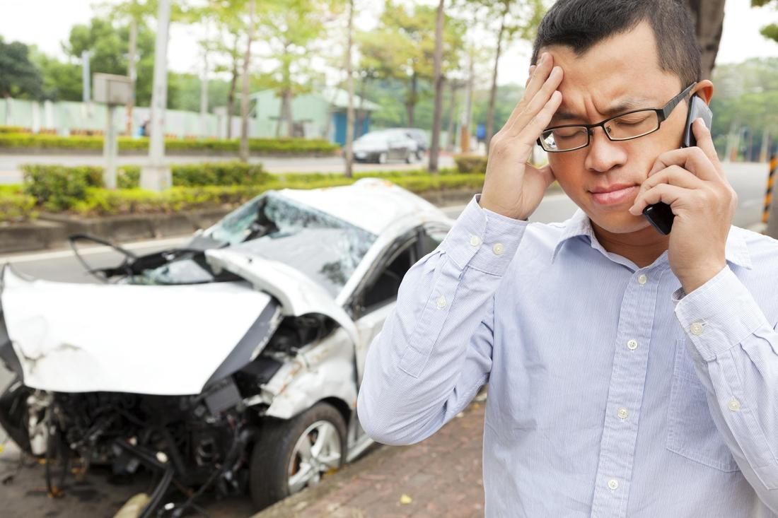 A man is talking on a cell phone in front of a damaged car.