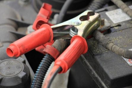 A close up of a car battery with jumper cables attached to it.