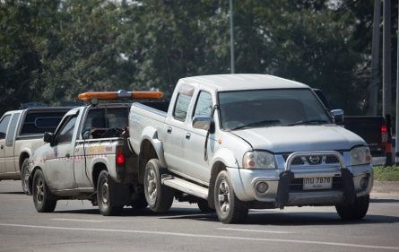 A tow truck is towing a pickup truck in a parking lot.