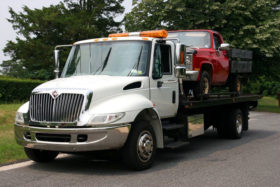 A white tow truck with a red truck on the back of it