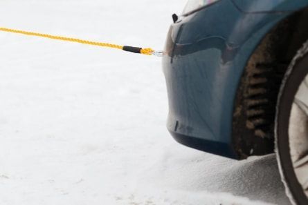 A car is being towed by a yellow rope in the snow.