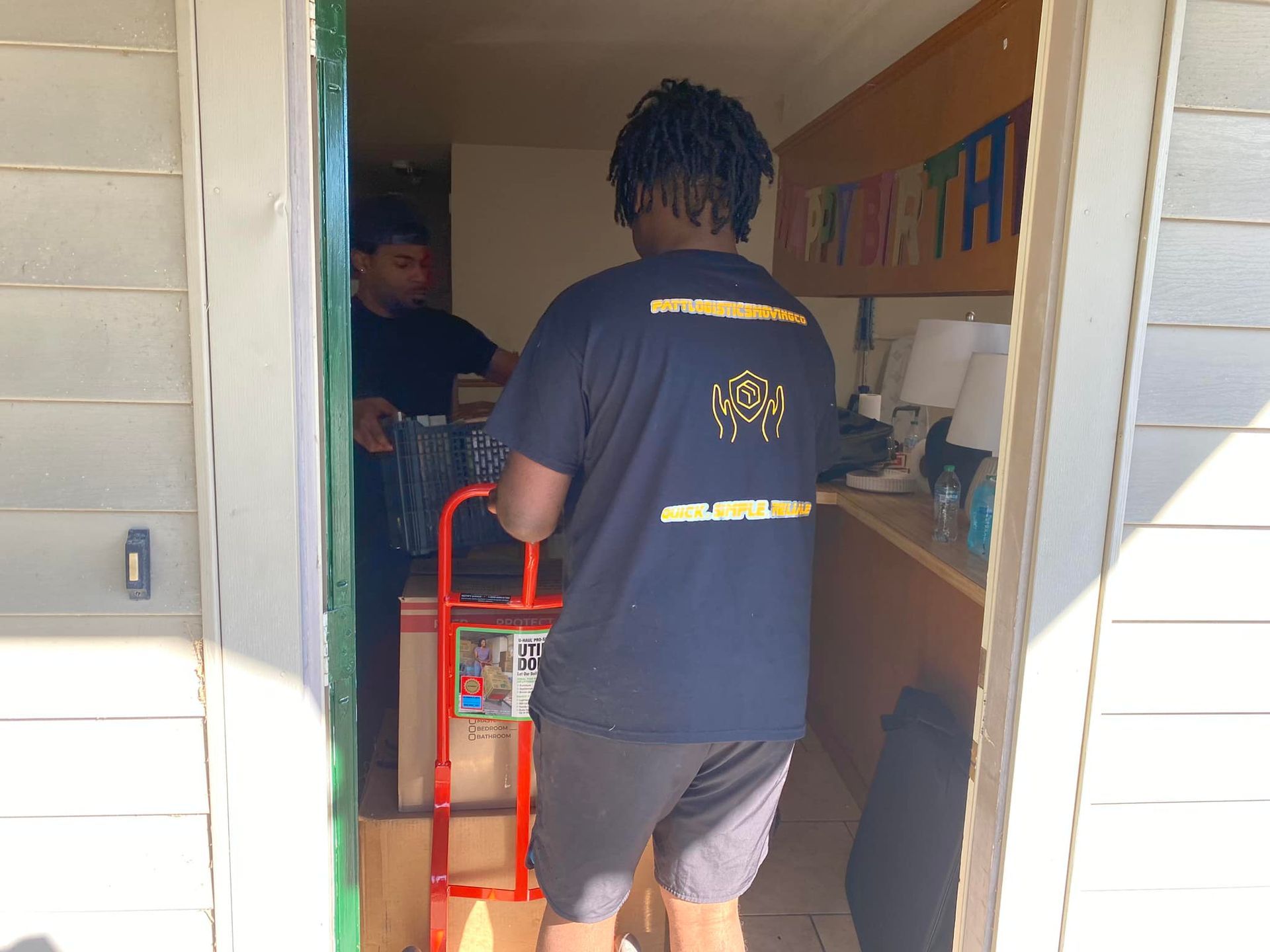 A man in a black shirt is pushing a dolly through a doorway