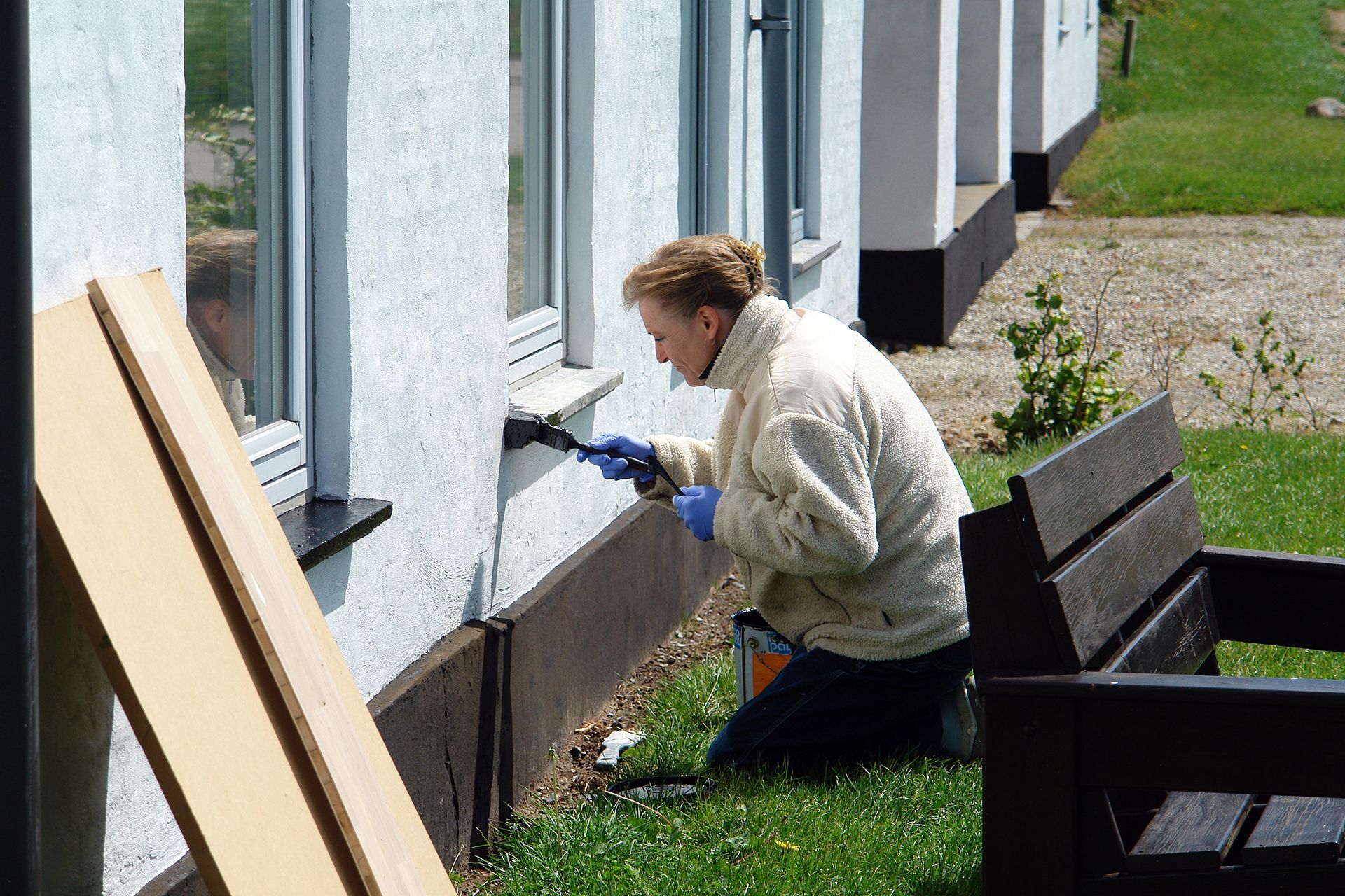 A woman is kneeling down painting a white wall