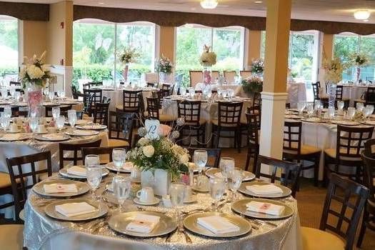 A banquet hall featuring multiple round dining tables with white tablecloths, floral centerpieces, and dark wood chairs.