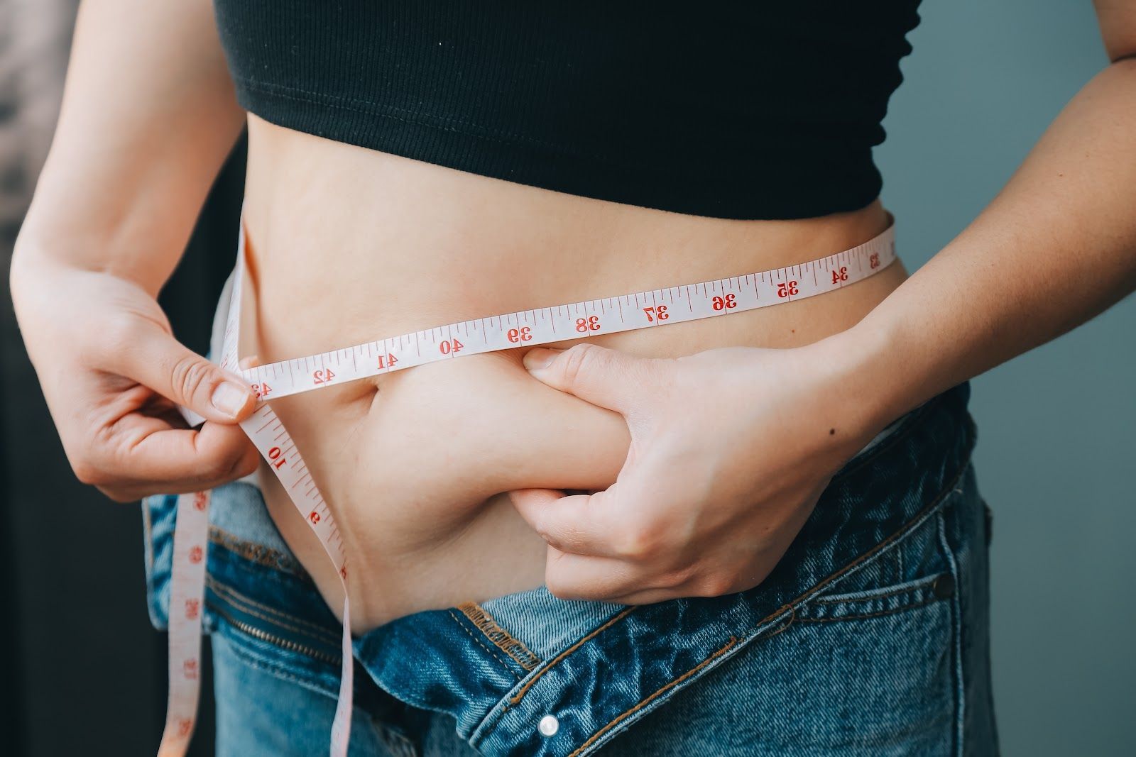 Person measuring waist circumference with a measuring tape.