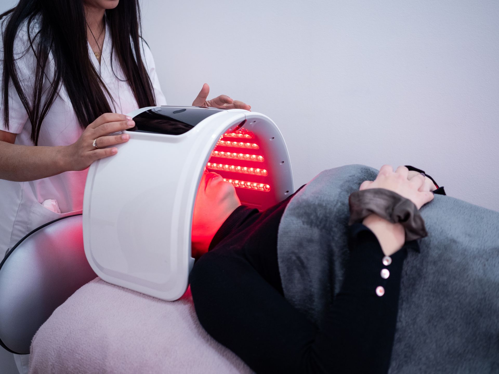 Woman undergoing red light therapy at a spa, with a technician adjusting the machine over her face.