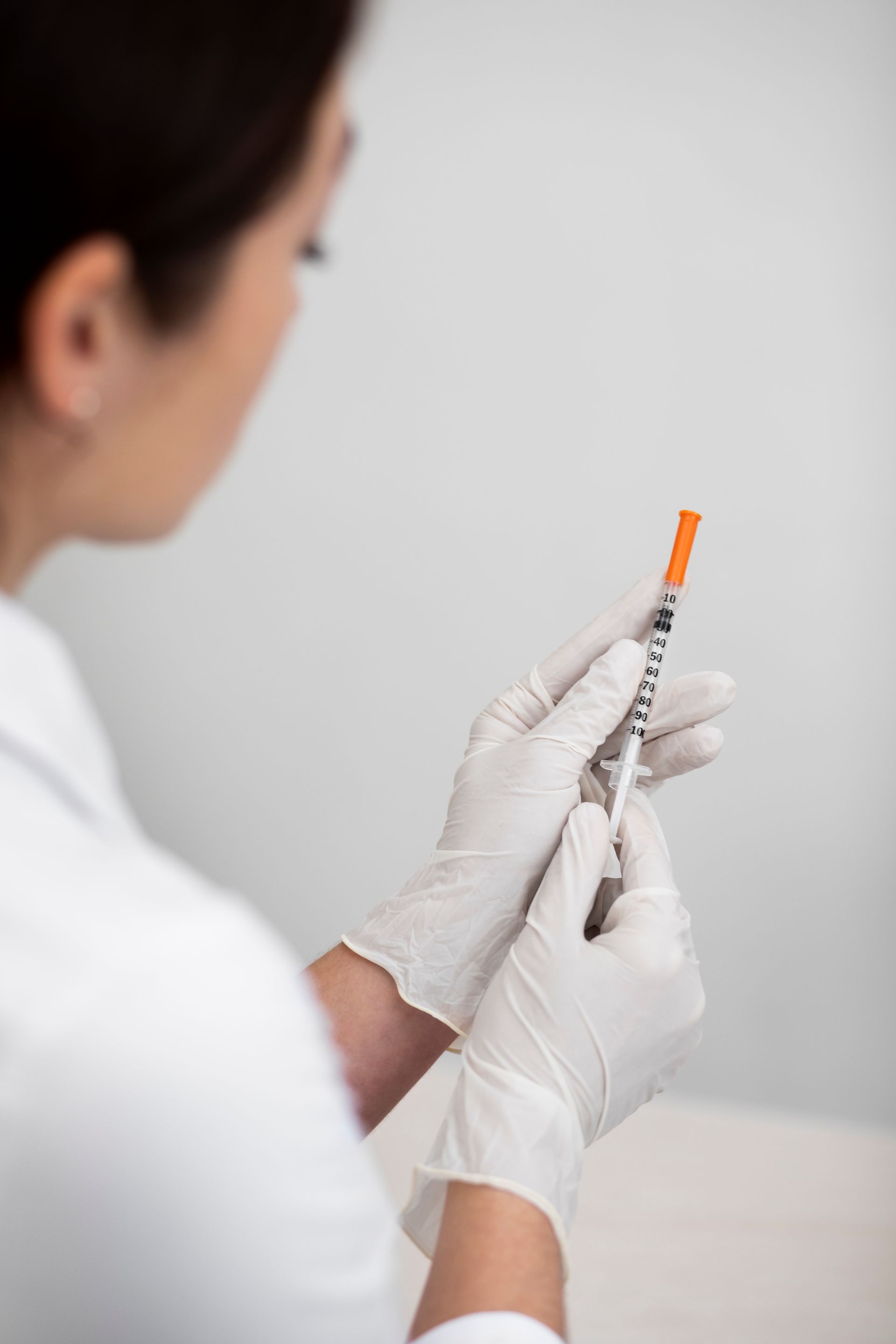 Medical professional in white coat and gloves preparing a syringe for injection.