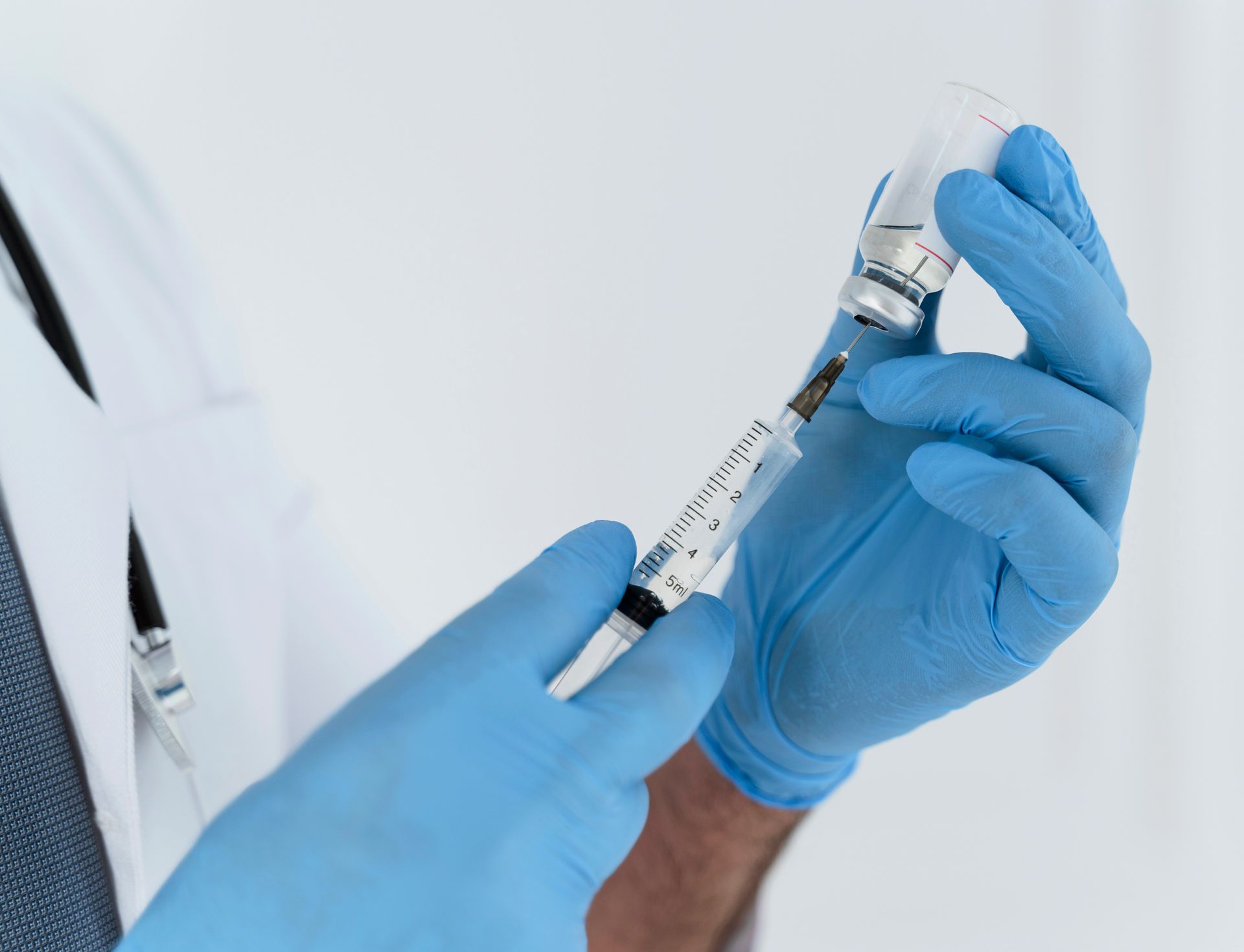 Doctor in blue gloves drawing vaccine from vial with syringe.