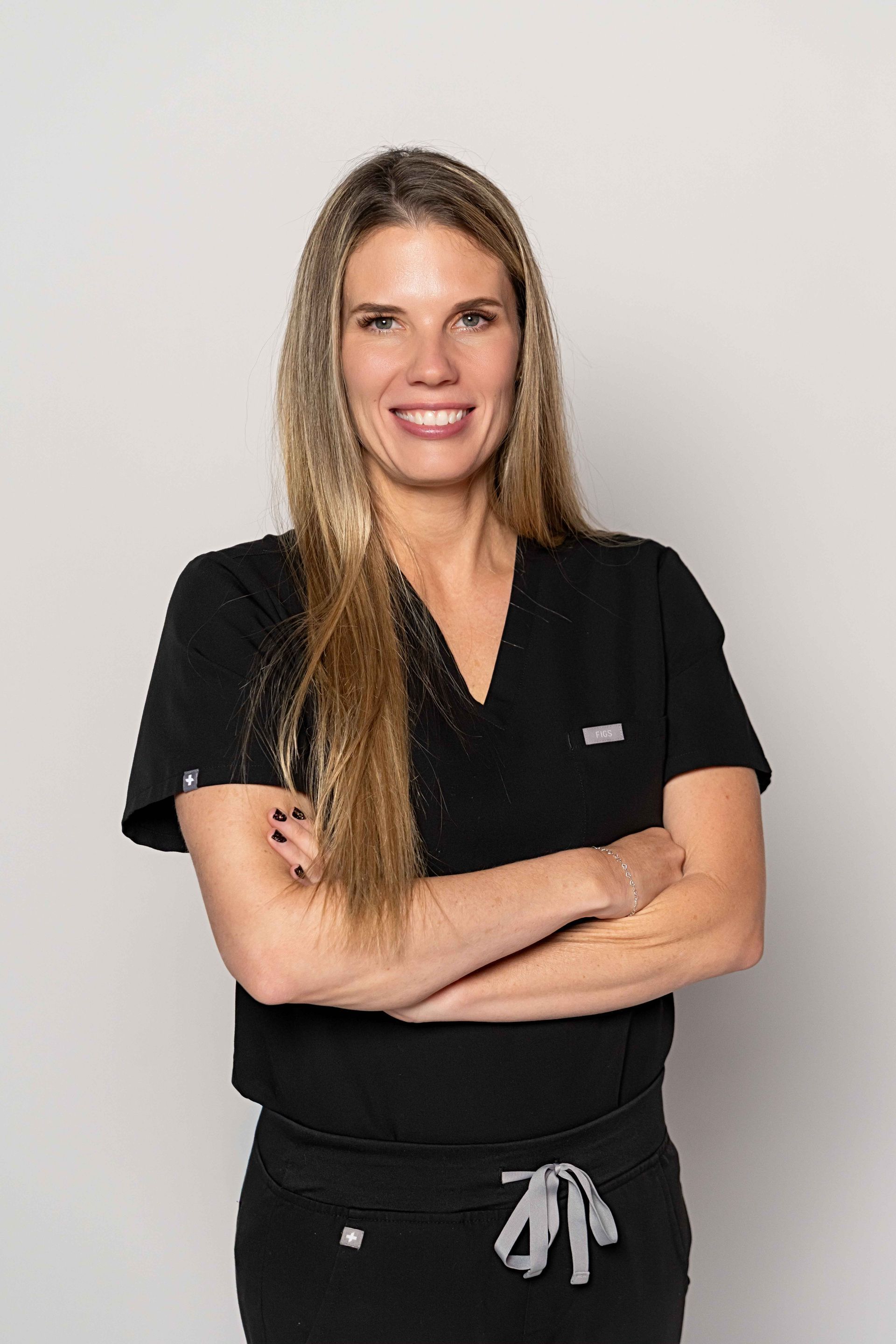 Woman in black scrubs with arms crossed, smiling, in front of a white background.