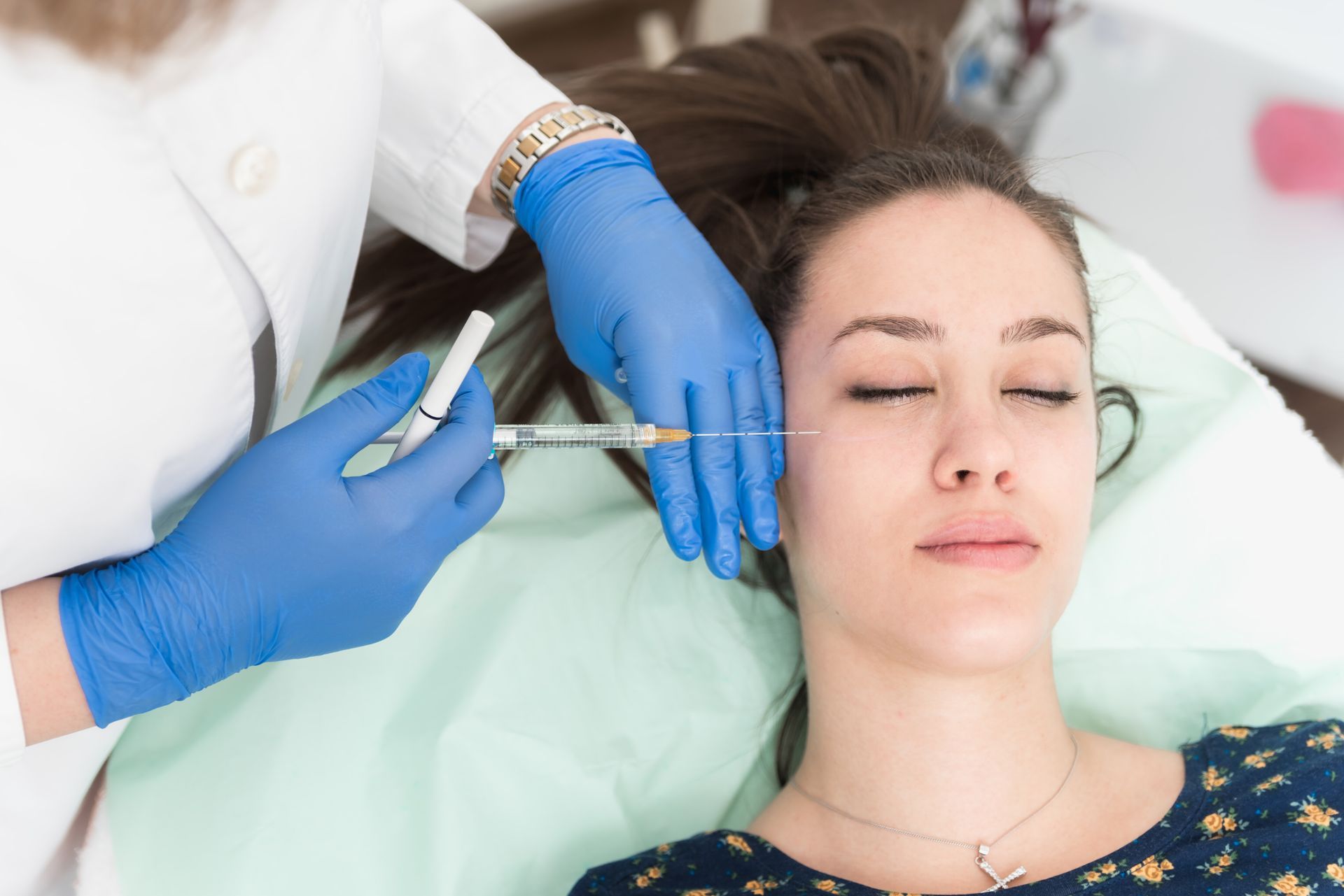 A person receives a facial injection from a gloved professional in a medical setting.