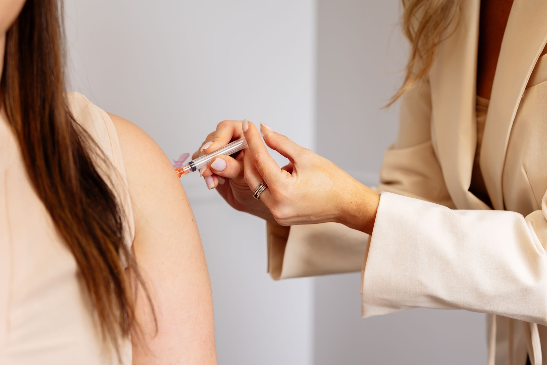 Woman receiving an injection in her shoulder by a person in a beige blazer.