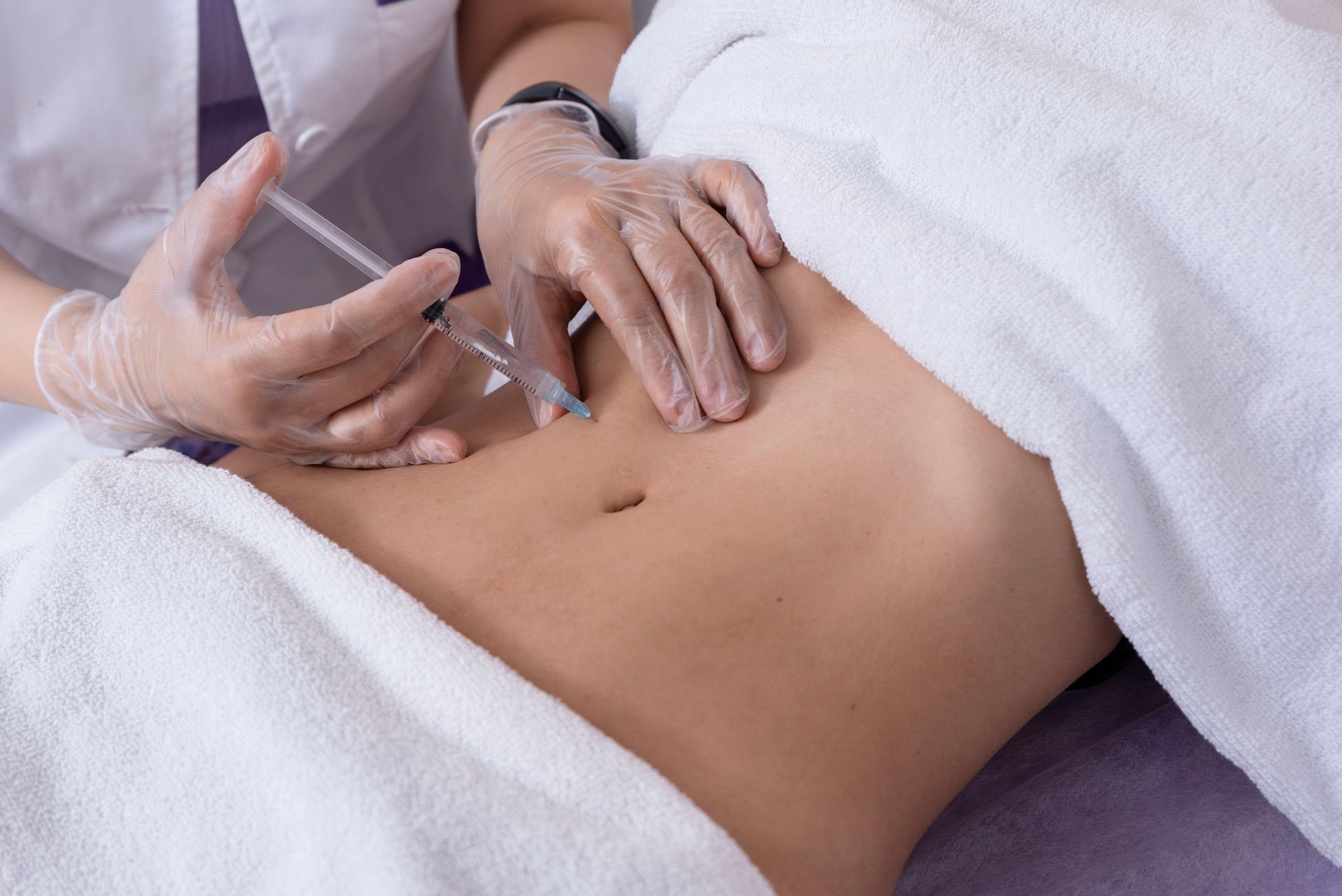 Person receiving injection in stomach, wrapped in white towel.
